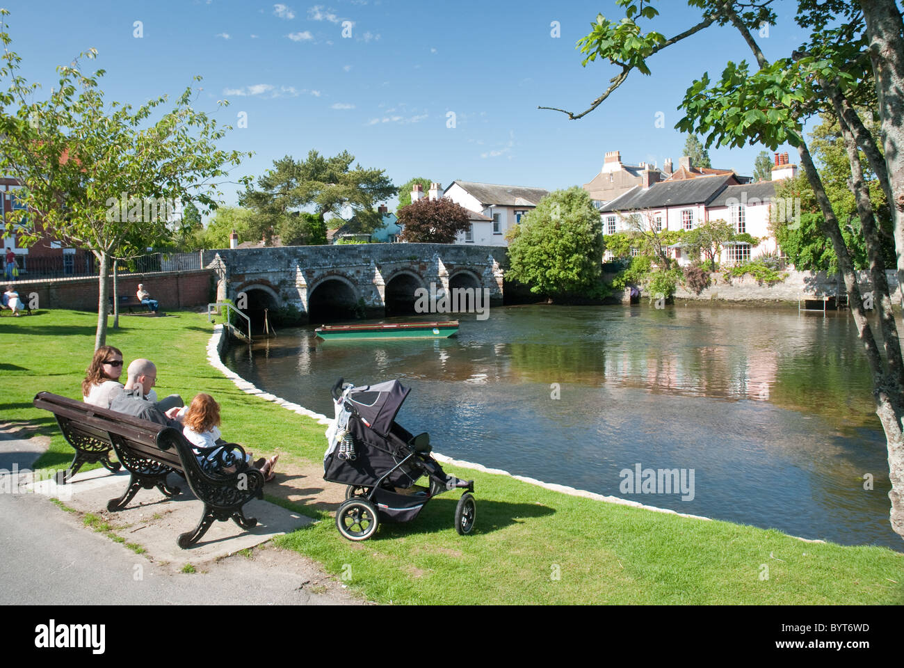 A group of people sit on a park bench near the Avon River in Christchurch, Dorset. Stock Photo