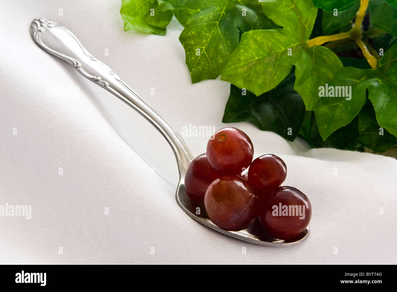 Red grapes piled on spoon on white cloth with leaves on background Stock Photo