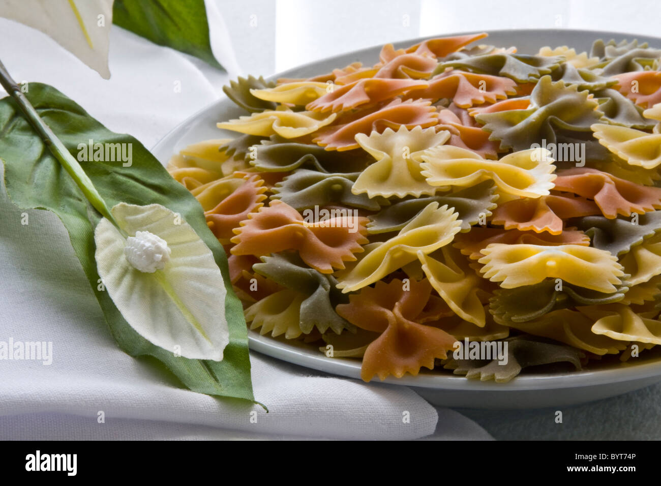 Tricolor farfalle pasta uncooked with flower, bowl and napkin Stock Photo
