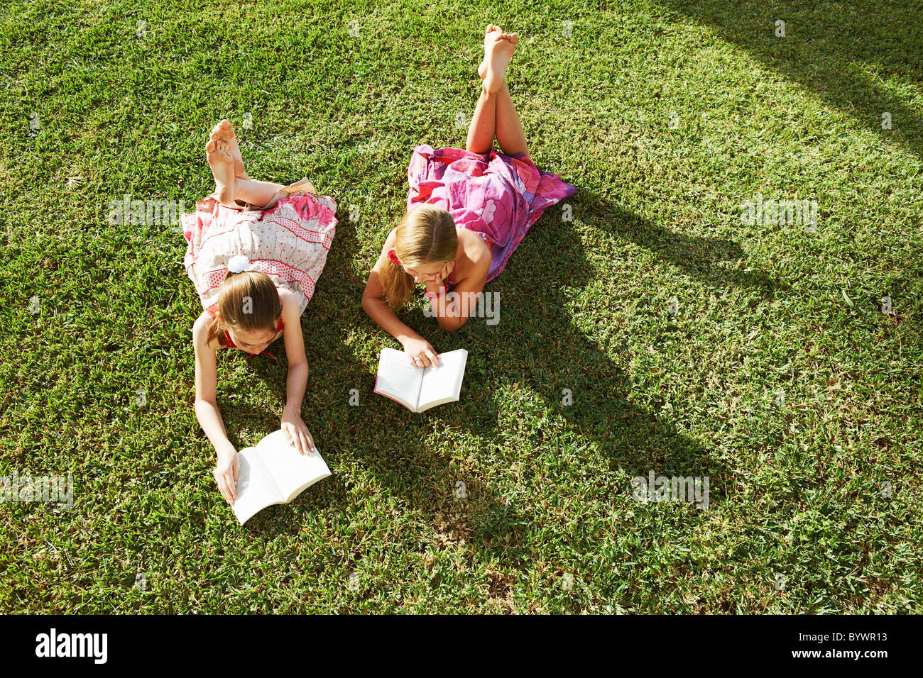 Girls lying on grass reading books Stock Photo