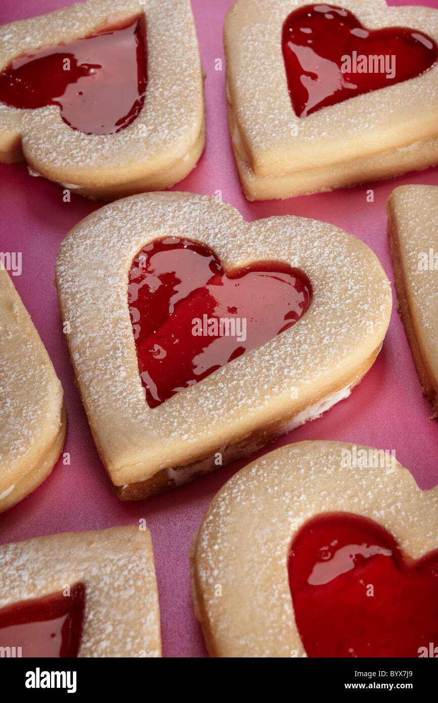 Close up photograph of a heart shaped biscuit on pink background, biscuit at an angle, biscuits in background Stock Photo
