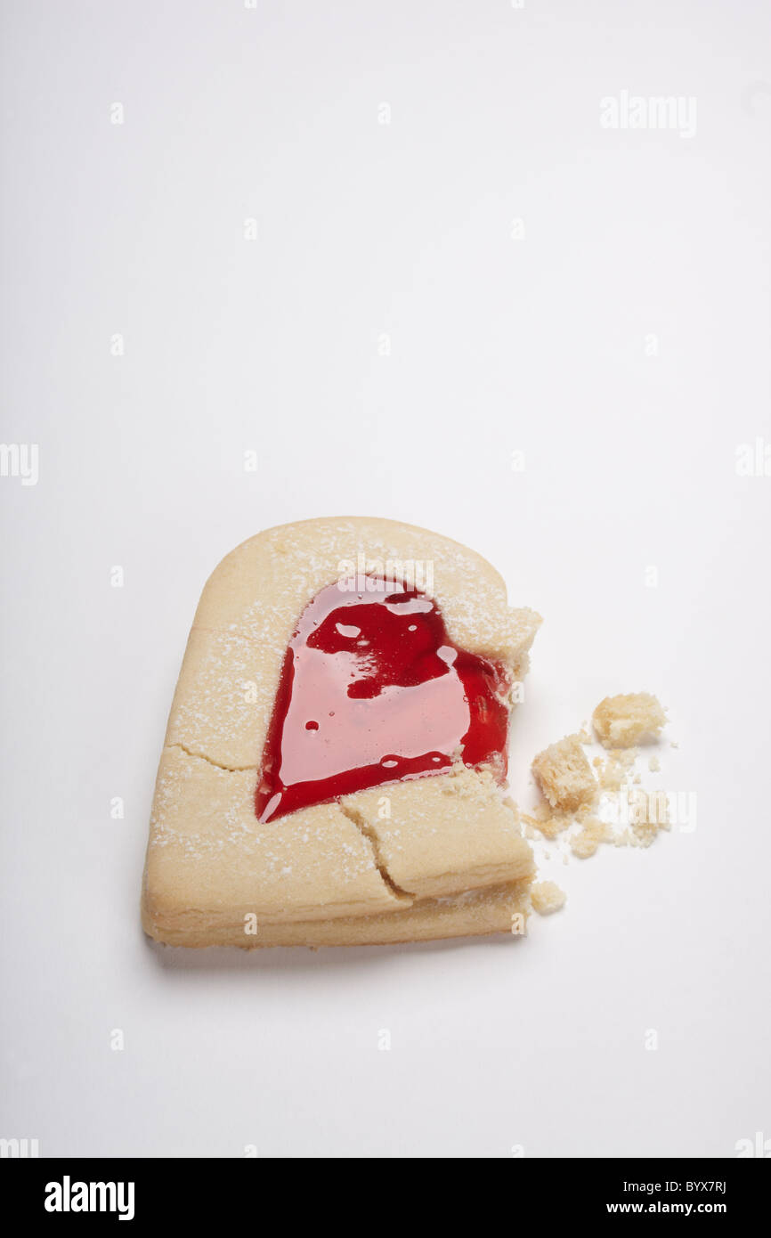 Photograph of heart shaped biscuits filled with red jam on a white background. Includes broken biscuit and crumbs. Valentine's day concept. Stock Photo