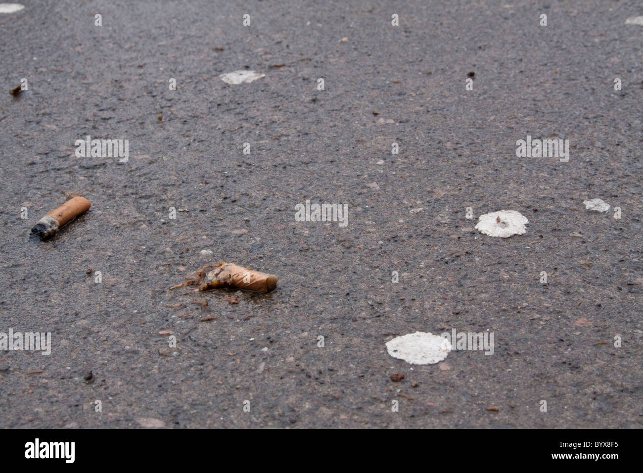 Discarded cigarettes and chewing gum stuck to the ground outside the entrance to a public building. Stock Photo