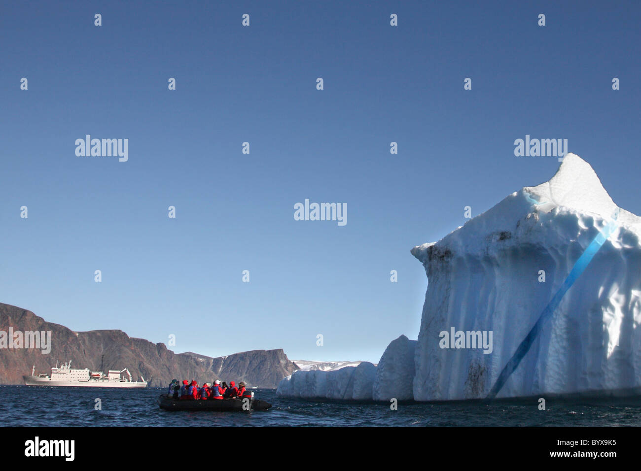 iceberg and tourists on an inflatable raft with their boat in the