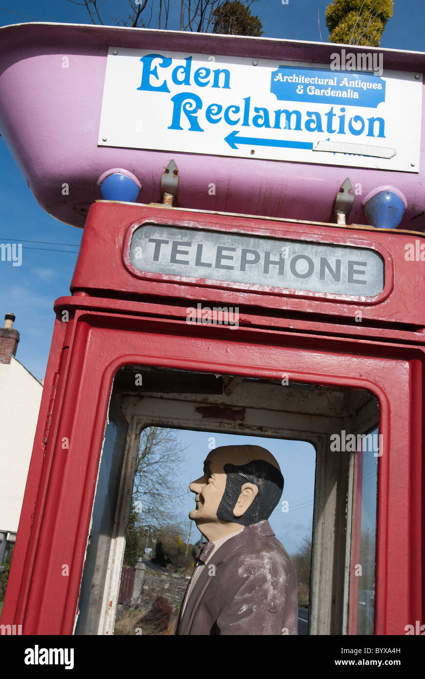 A British UK telephone box at a reclamation centre, St Austell, with a dummy inside and a pink bath atop! Stock Photo