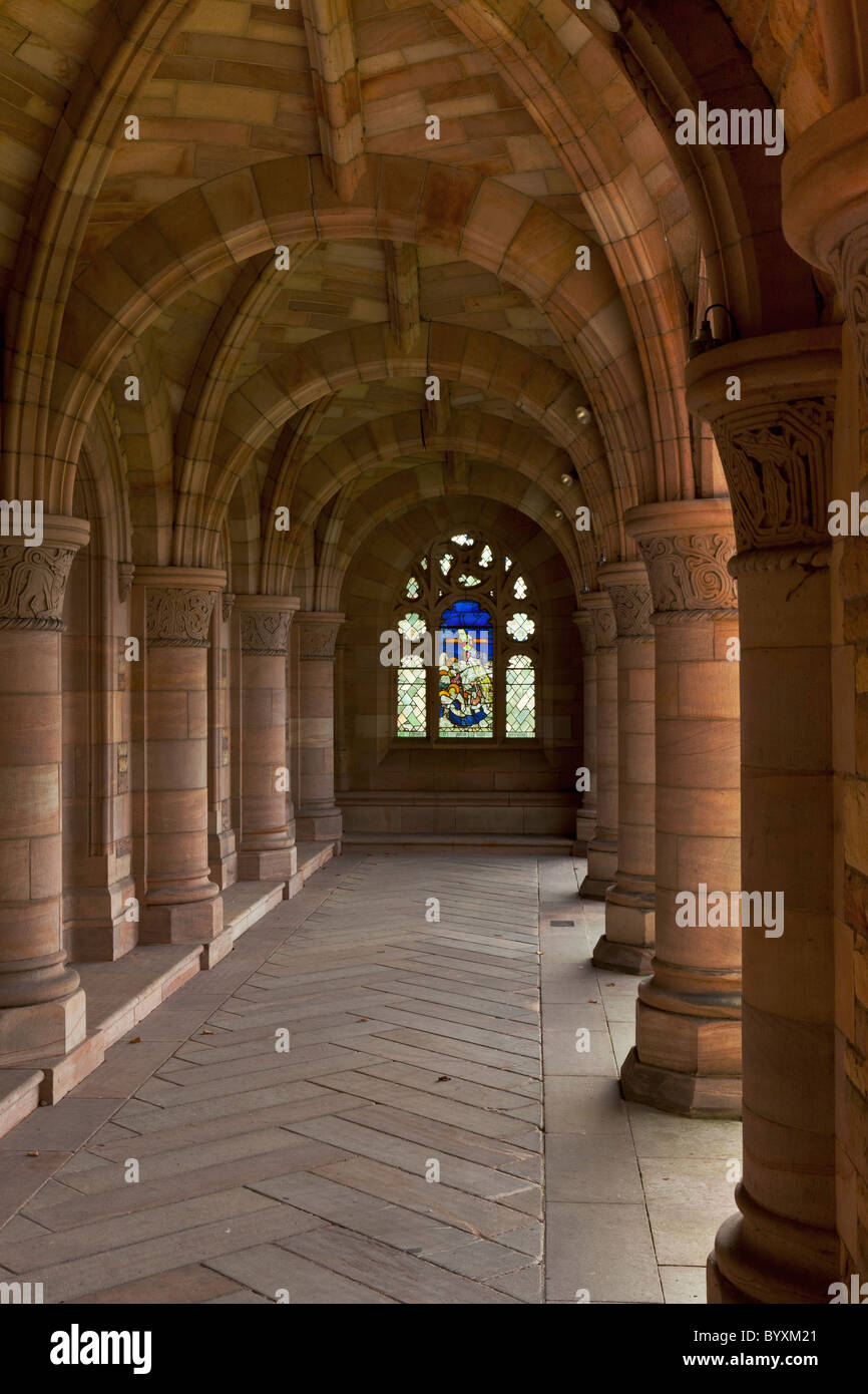 a stained glass window at the end of an outdoor corridor with arches and columns; scottish
