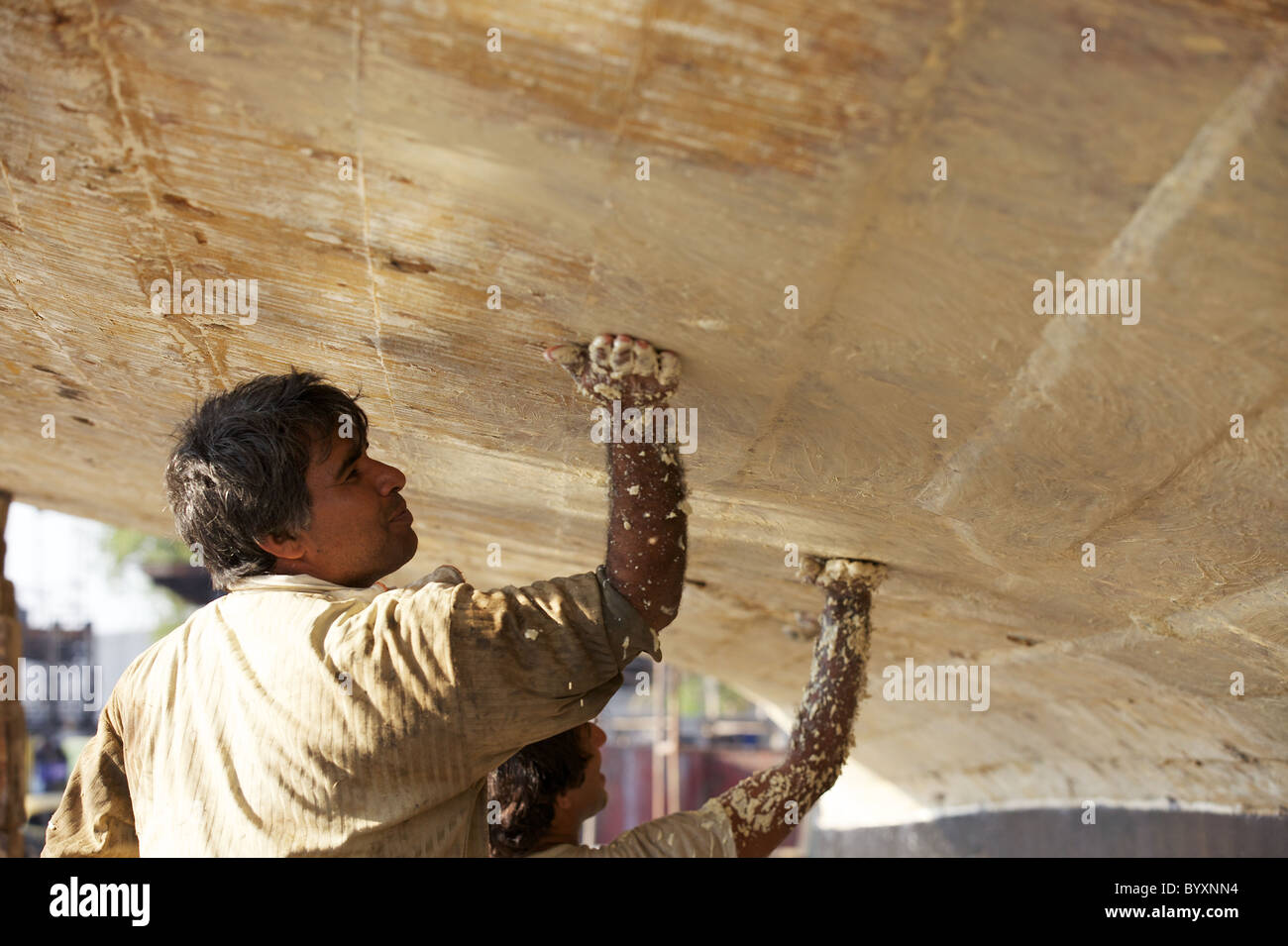 Two workers apply a sealer to the underside of a dhow in the Jaddaf boatyard, Dubai, UAE Stock Photo