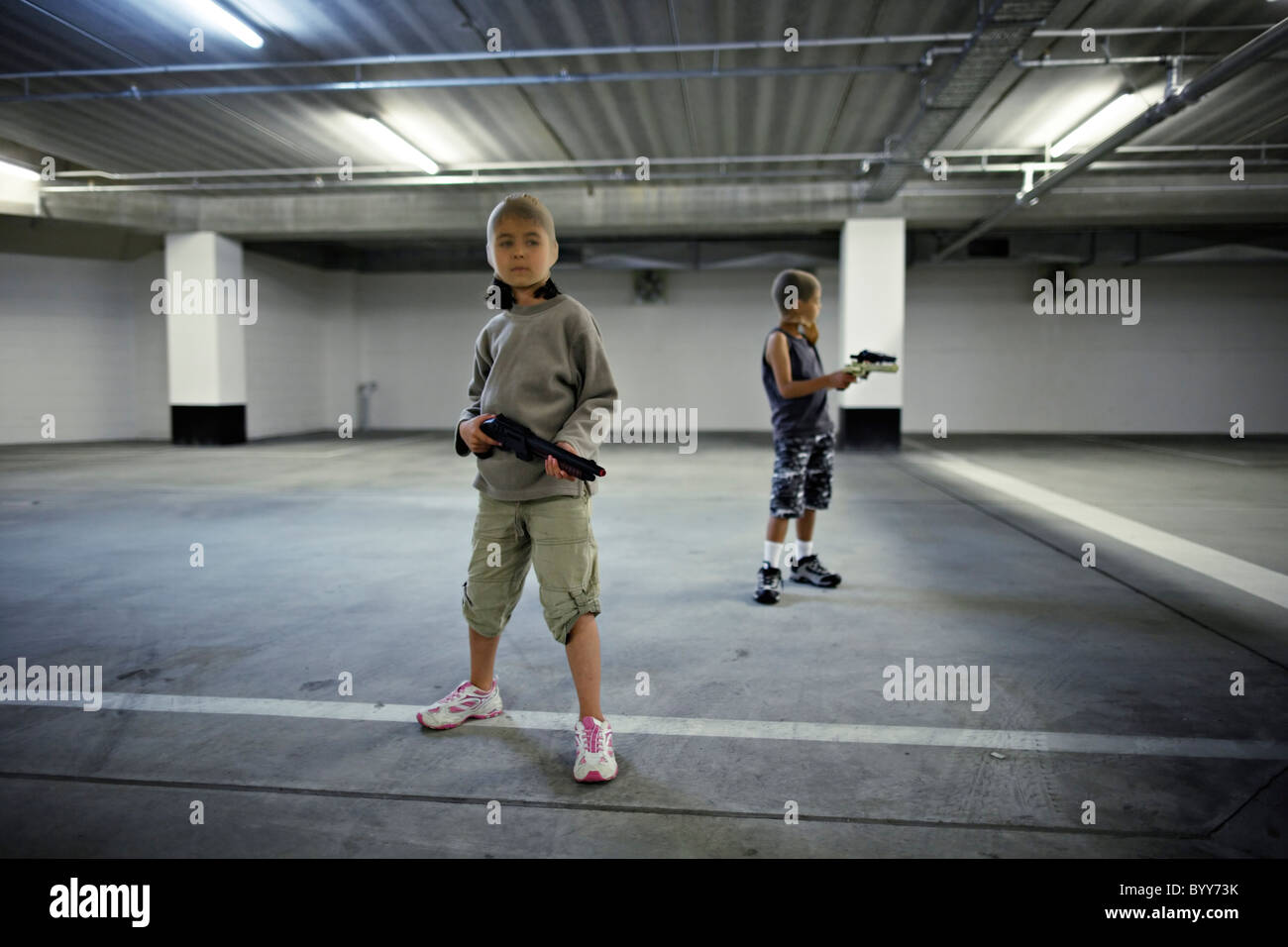 Children with stocking masks and toy guns in underground carpark prepare for big hold-up. Stock Photo