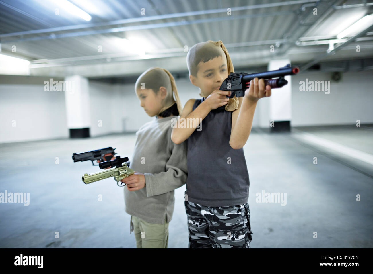 Children with stocking masks and toy guns in underground carpark prepare for big hold-up. Stock Photo