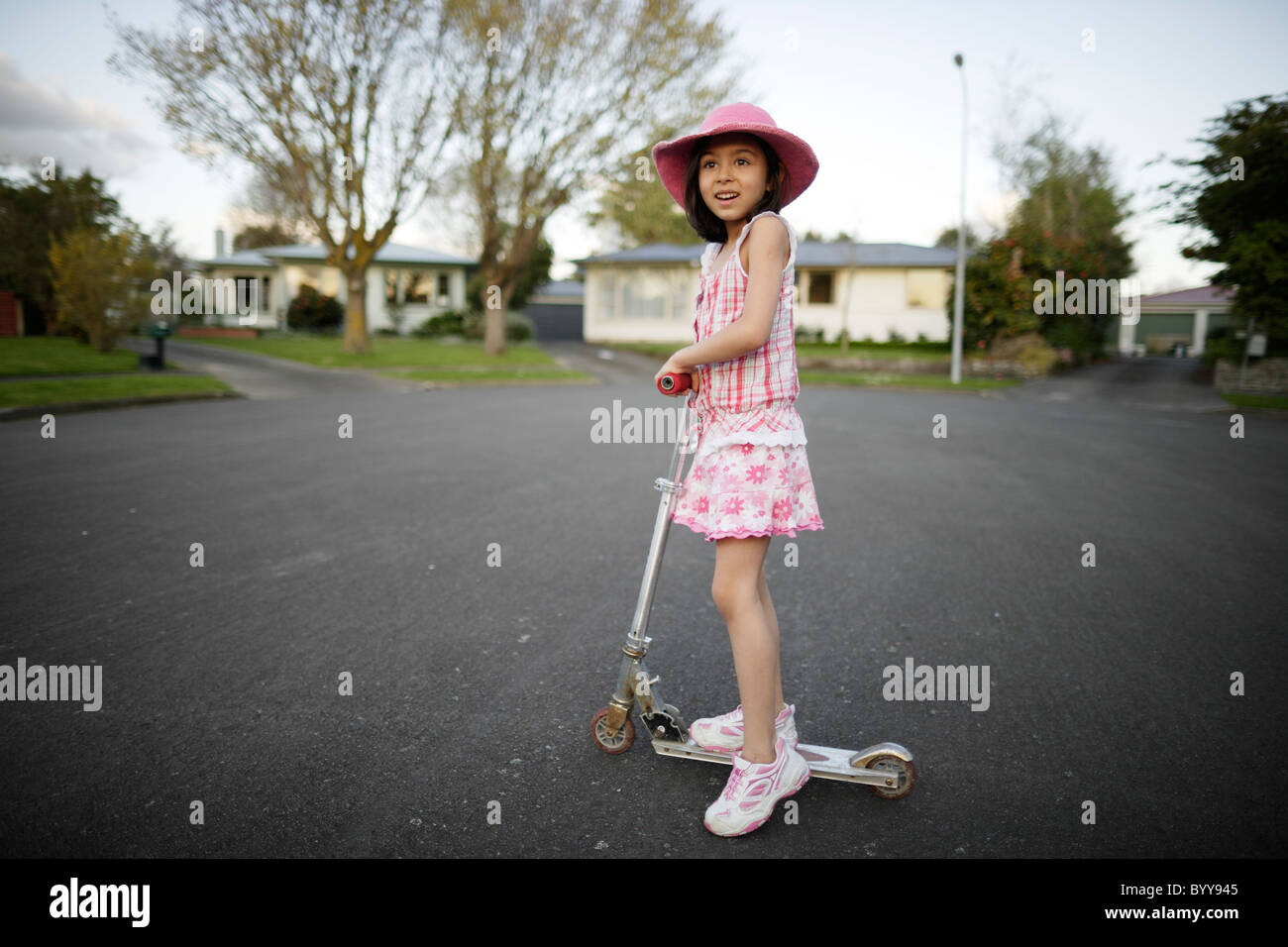 In my street. Girl rides scooter at end of culdesac, New Zealand. Stock Photo
