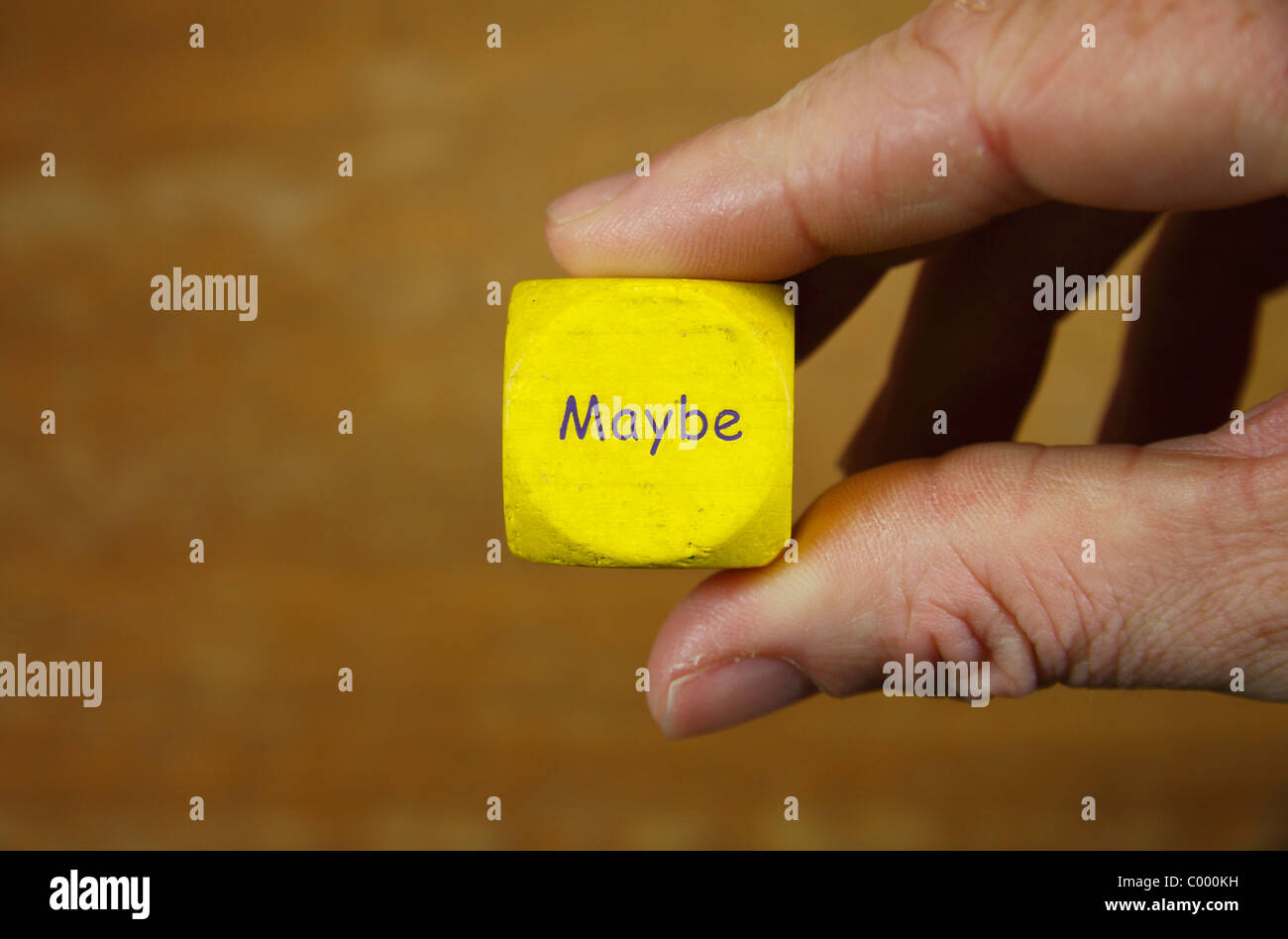 A man holding a yellow dice with the word 'MAYBE' inscribed upon it. Stock Photo