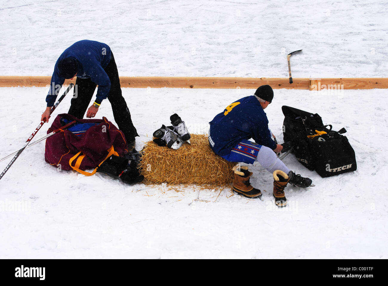 Players unpack hockey bag of gear at edge of outdoor ice rink. Stock Photo