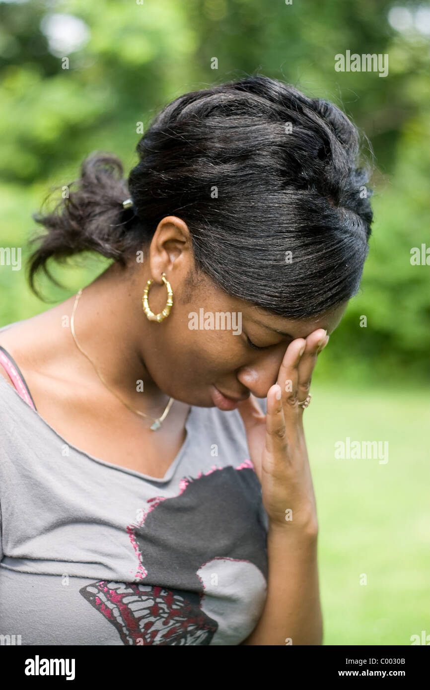 A young woman holds her hand on her forehead in anguish over pain or stress she is experiencing. Stock Photo