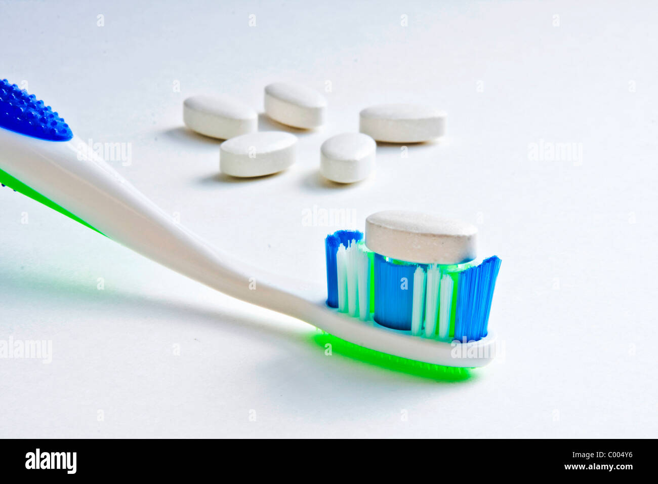 Calcium tablet resting on toothbrush bristles with other tablets in background Stock Photo