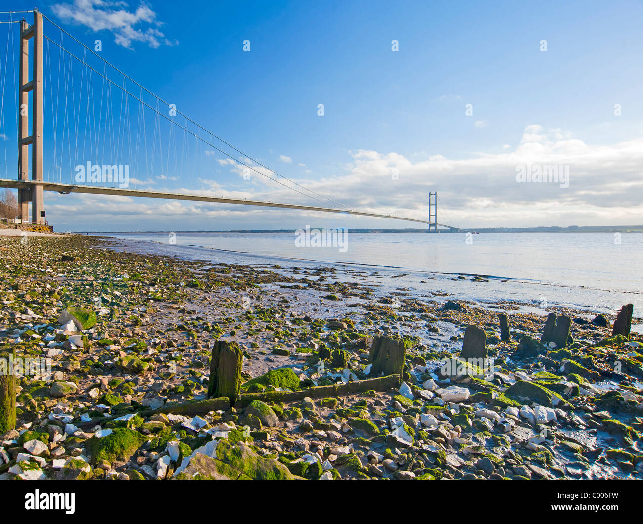 Large suspension bridge spanning a wide river with rocky beach foreground Stock Photo