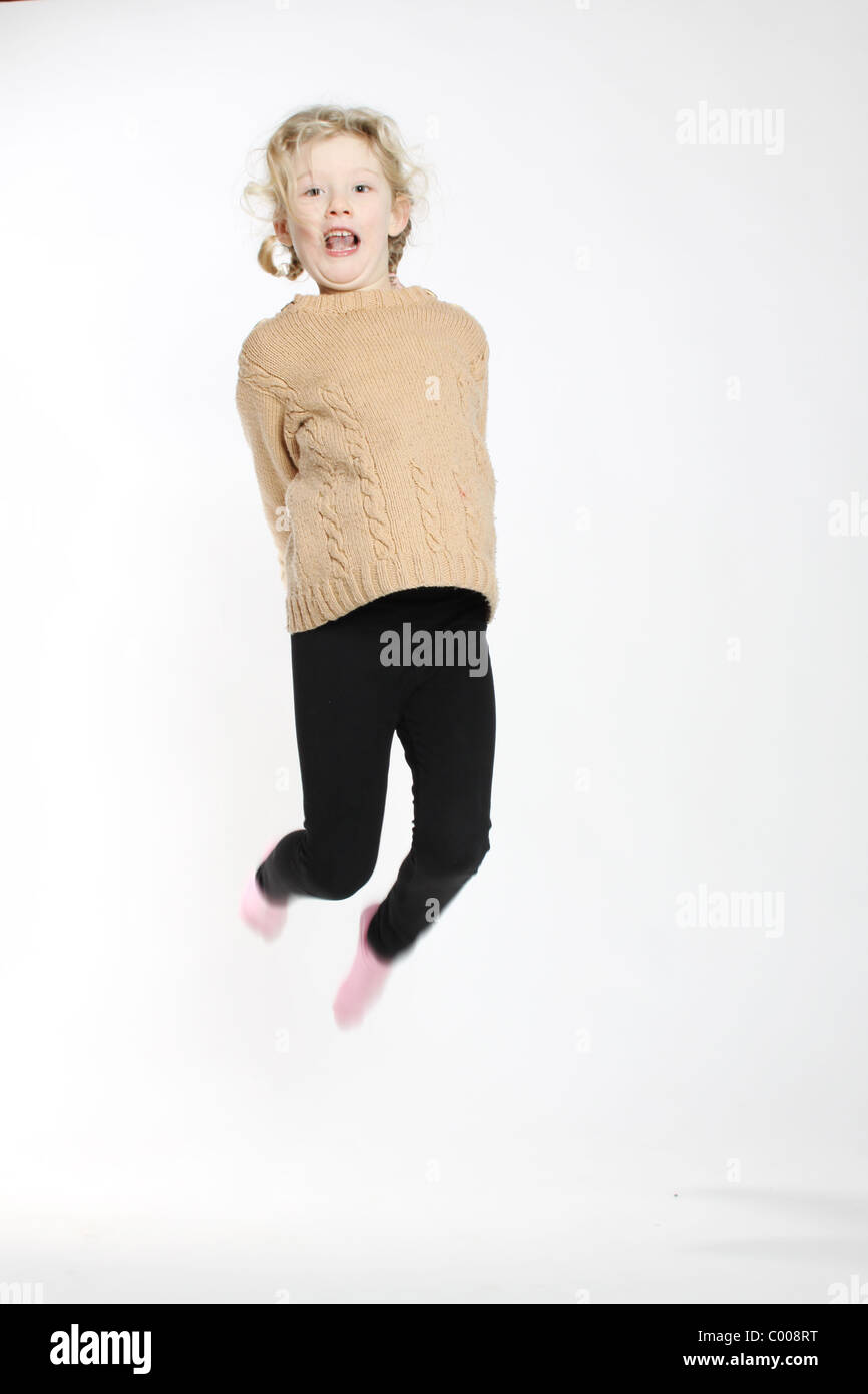 A blond white girl with bunches, jumping wearing a brown jumper and black leggins Stock Photo
