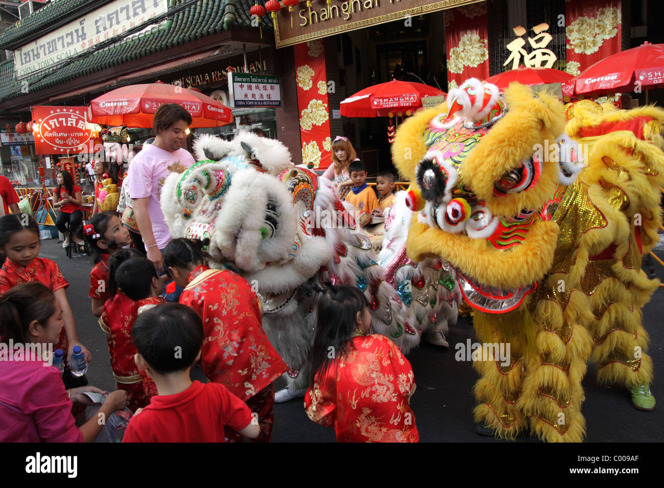 Children playing with Chinese lion dance performers celebrate the Chinese new year in a street in Bangkok Stock Photo