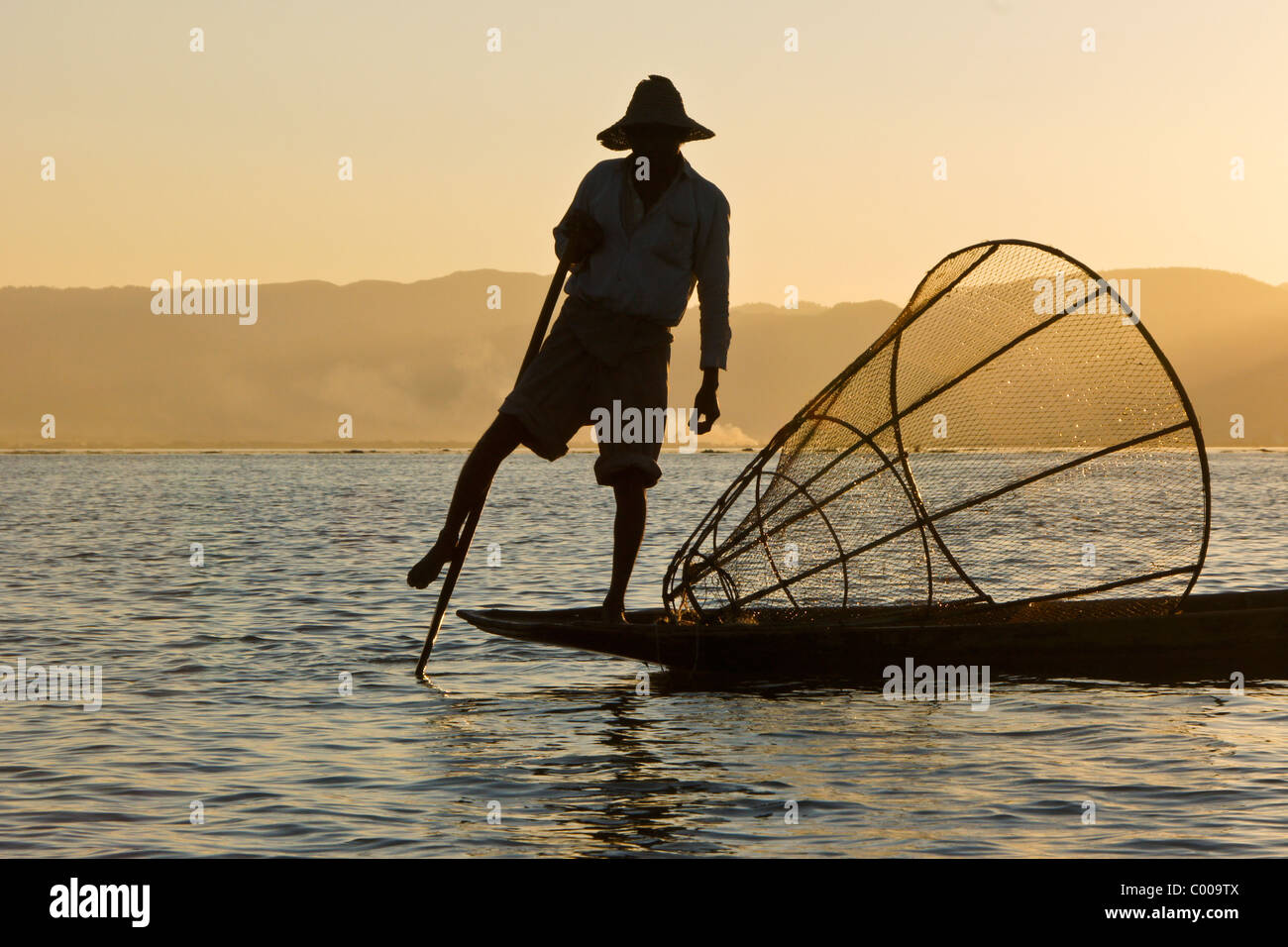 Intha legrowing fisherman with basket net on Inle Lake at sunset
