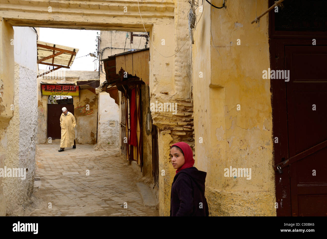 Moslem man in jellaba and white cap with young girl in yellow Fes el Bali Medina Morocco Stock Photo