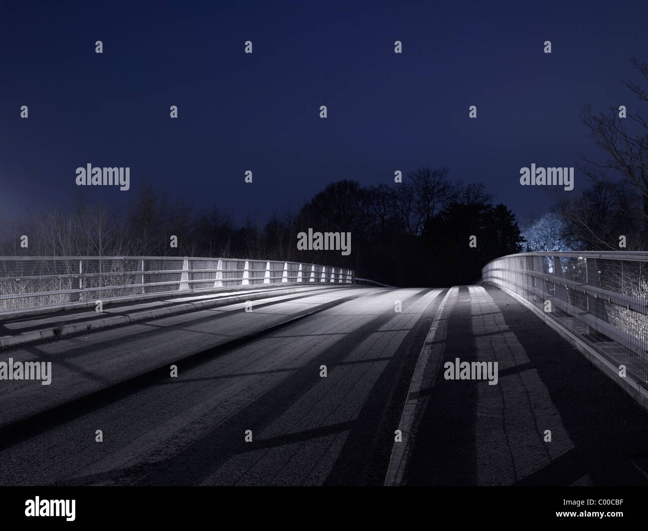 Road and trees lit by street lights at night with blue sky , taken by roadside locations Stock Photo