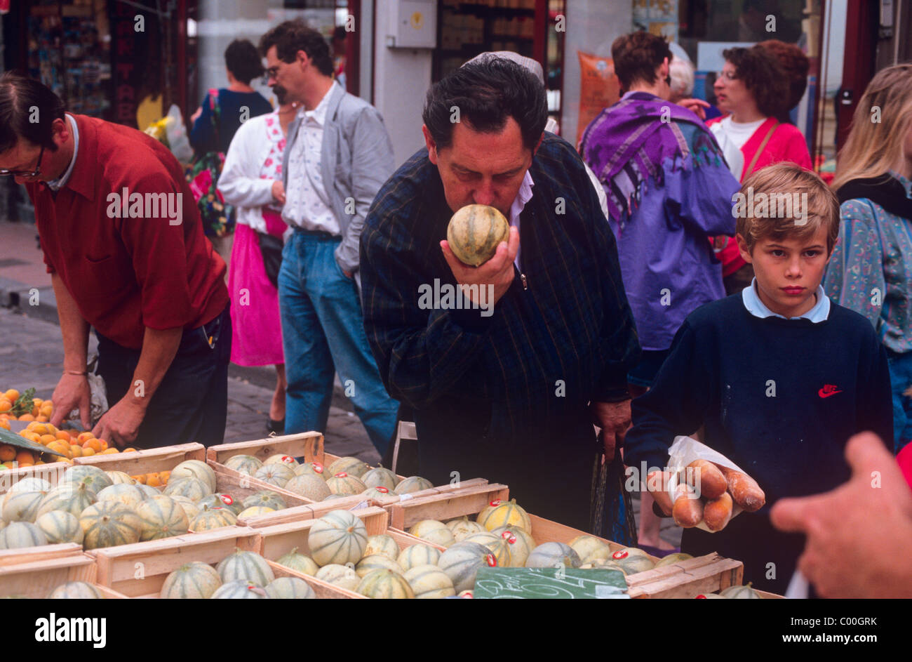 A man at a food market in France smelling a melon to test its ripeness