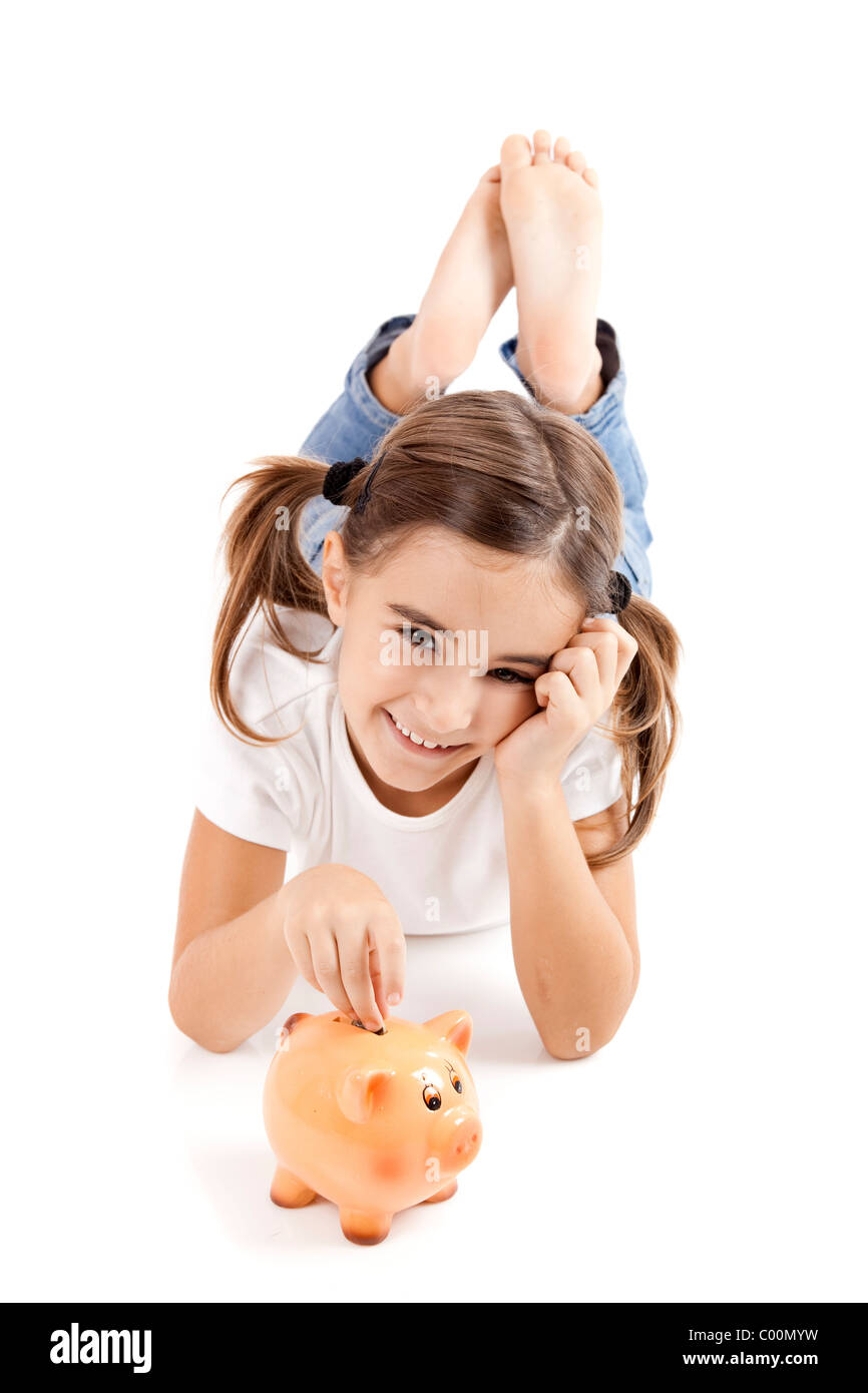 Little girl lying on floor and inserting a one euro coin on the piggy ...