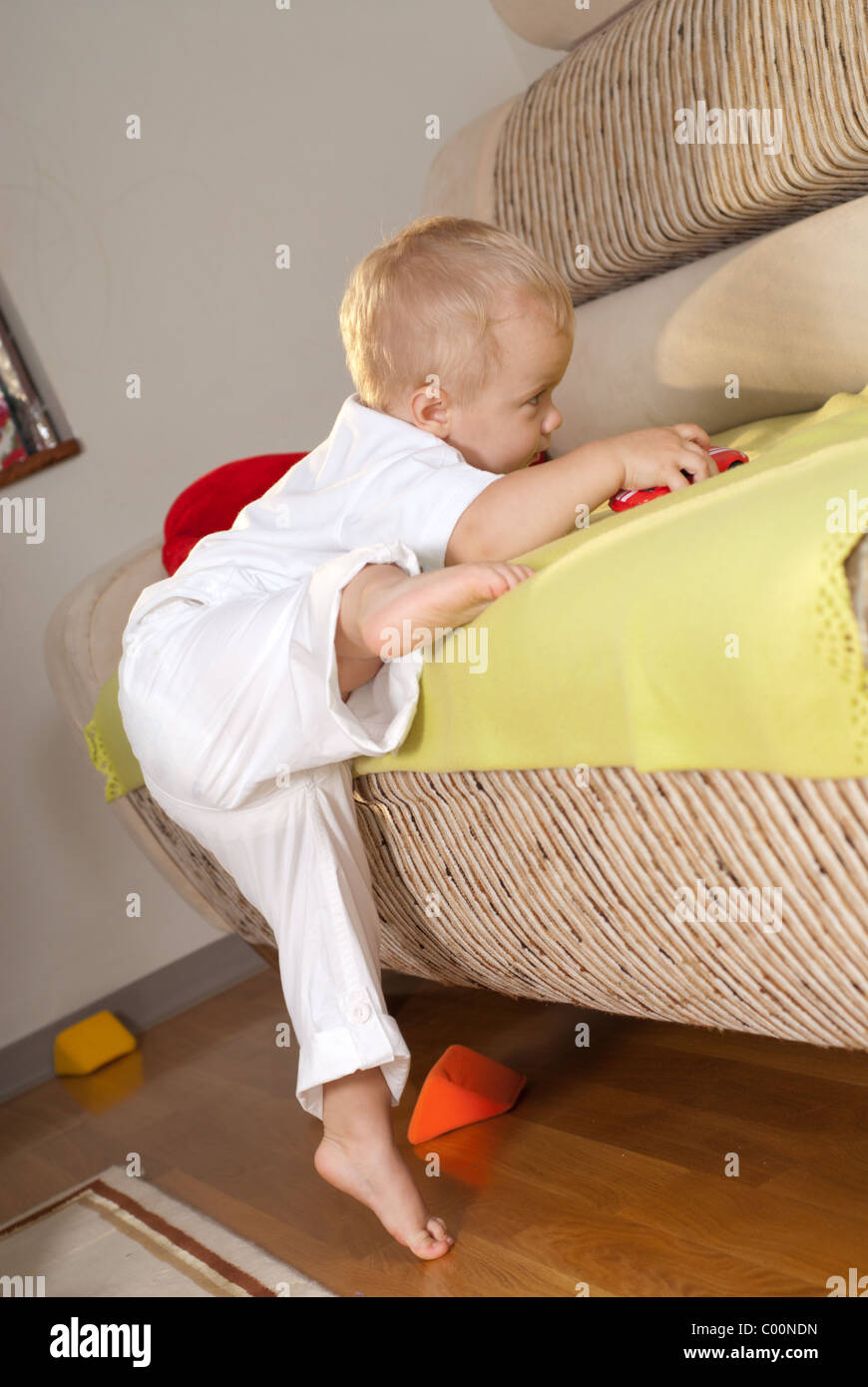 Little boy in white is climbing on sofa Stock Photo Alamy