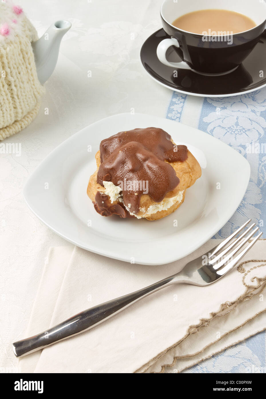 Afternoon Tea with chocolate covered choux pastry bun. Stock Photo