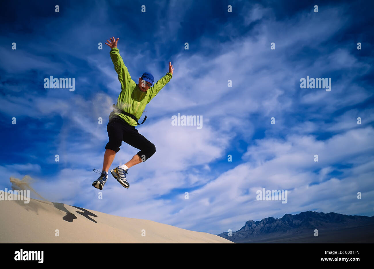 Hiker leaps from the summit of the Kelso Sand Dunes. Stock Photo