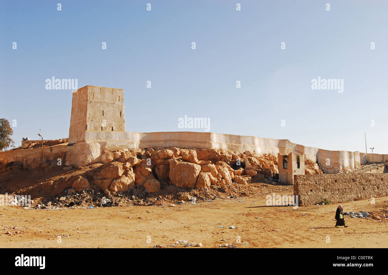 Algeria. Ghardaia, person walking on an arid landscape and a structure with rocks in the background Stock Photo