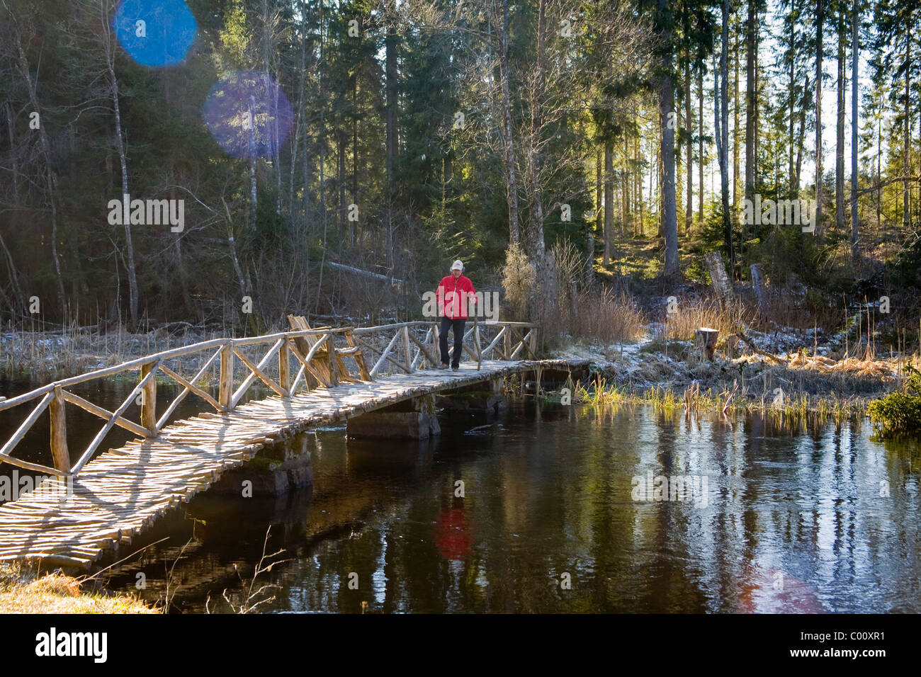 Man in red jacket walking on wooden bridge Stock Photo