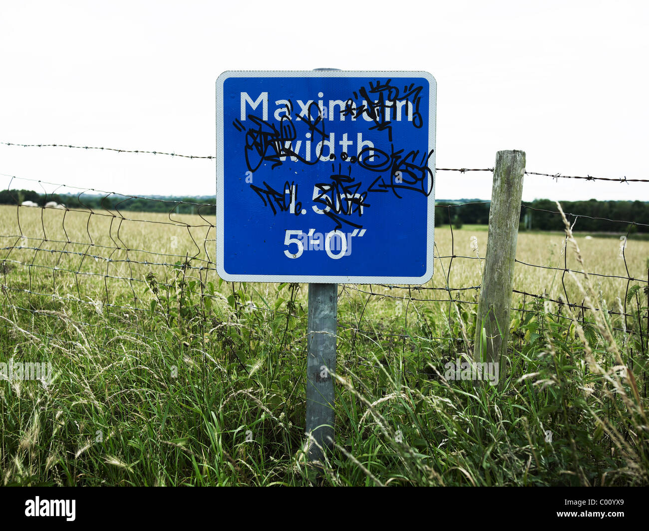 graffiti sign for small lane in cheshire village, vandalized and tagged sign says maximum width 1.5m or 5ft fields background Stock Photo