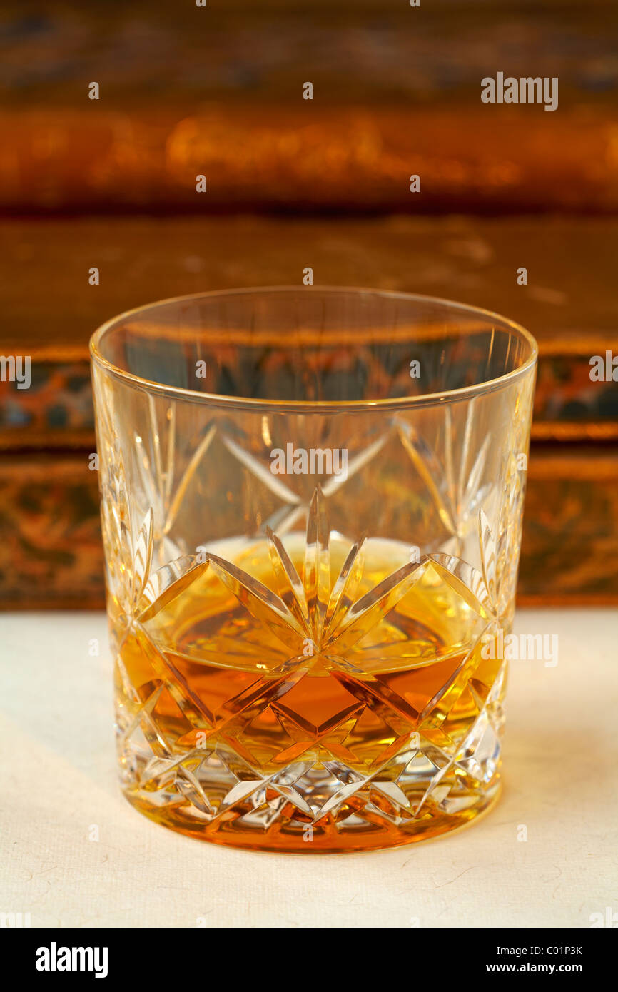 Cut glass tumbler of malt whisky and old antique leather books background Stock Photo