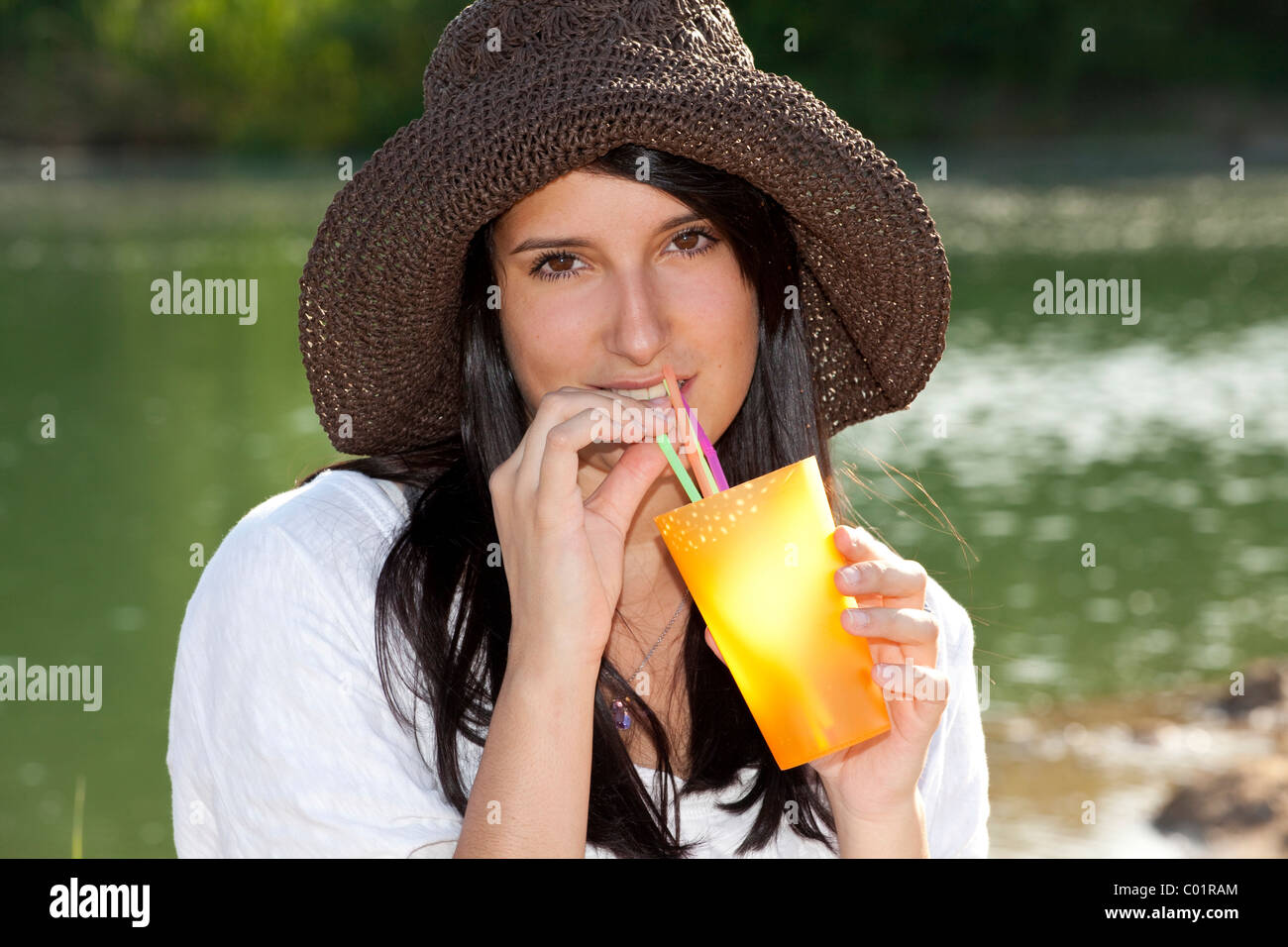Young woman wearing a straw hat sitting on the beach of a lake and ...