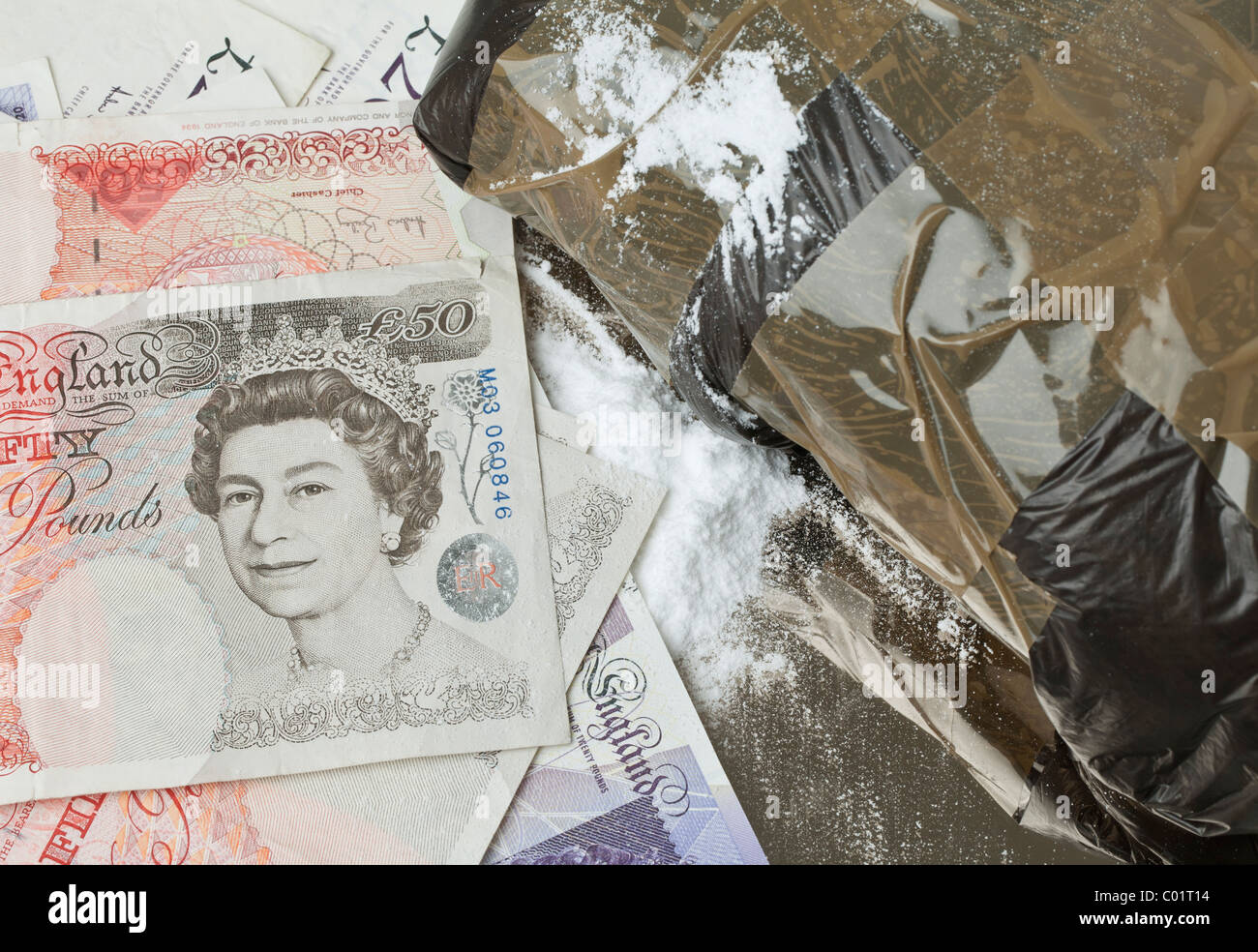 a black plastic packet sealed with brown tape containing white powder (drugs) on  a mirror together with some English bank notes Stock Photo
