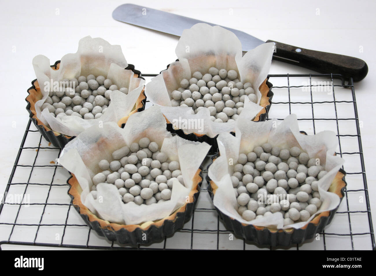 Empty pastry cases on a cooling tray with baking beans after being