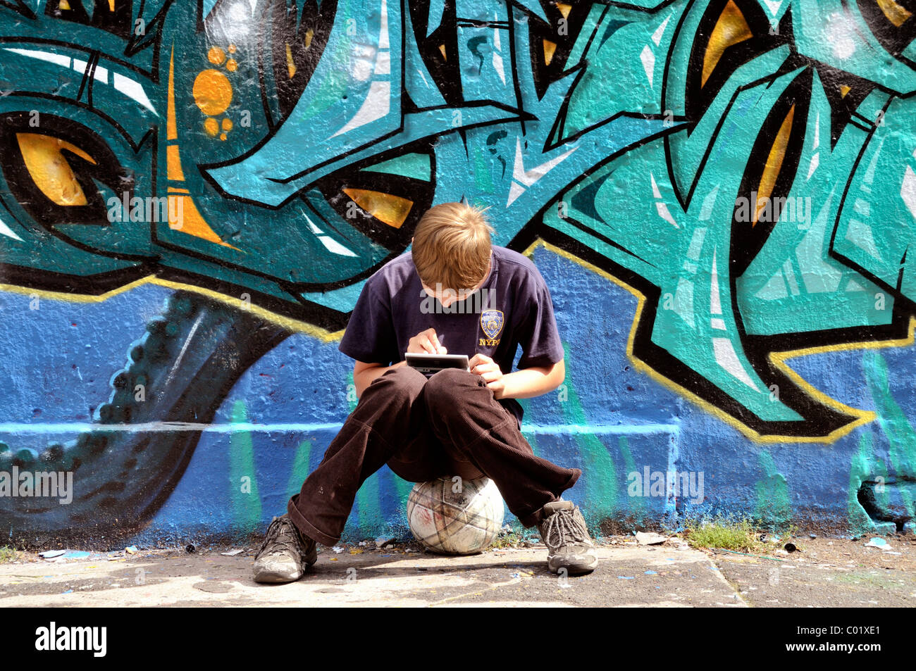 Ten-year-old boy playing with his Nintendo in front of a graffiti wall, Germany, Europe Stock Photo