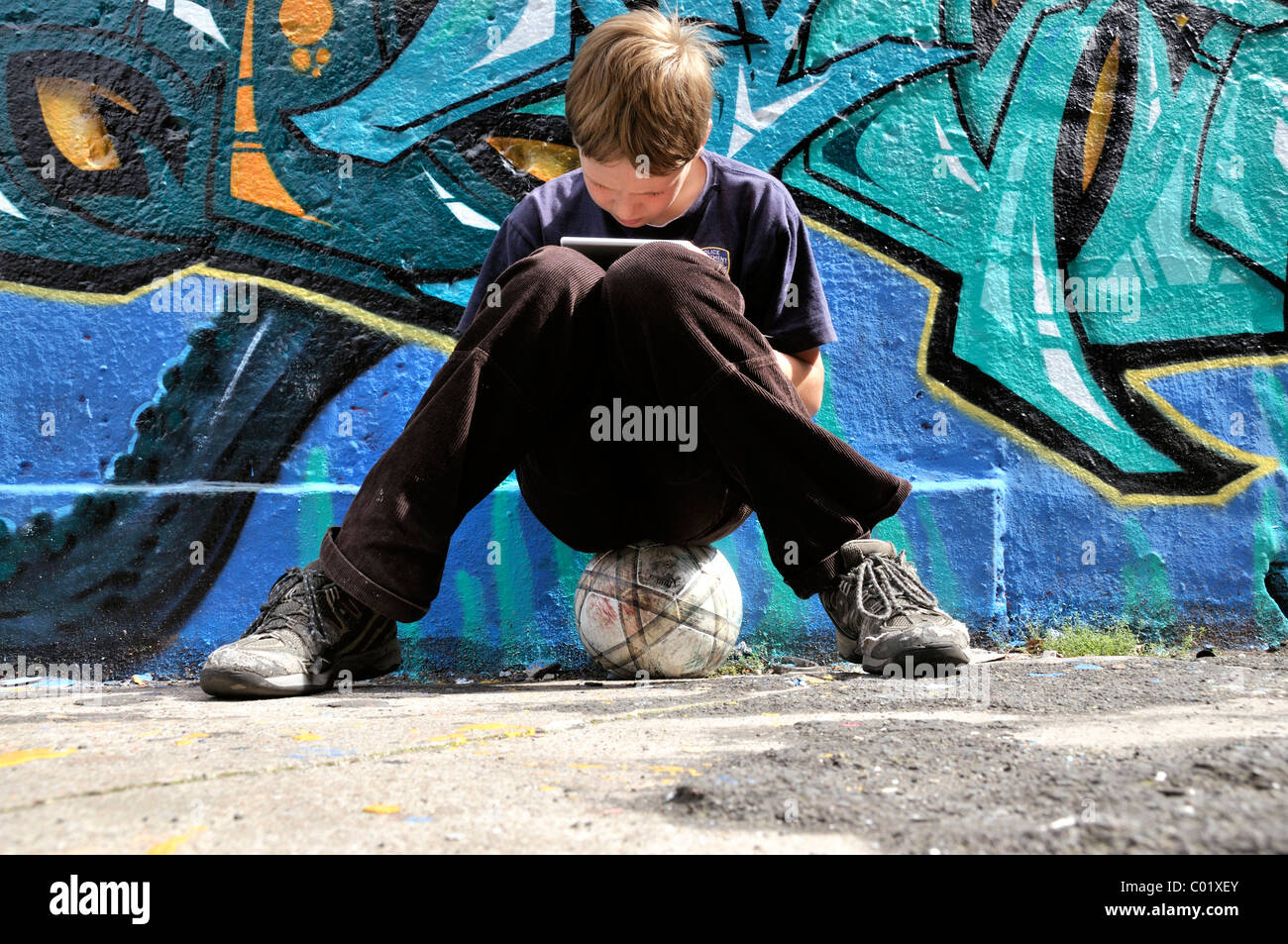 Ten-year-old boy playing with his Nintendo in front of a graffiti wall, Germany, Europe Stock Photo