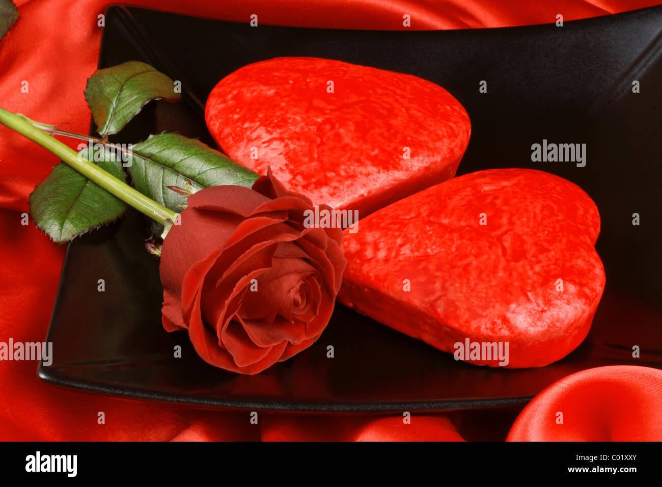 Two red heart shaped cakes on a black plate over a red background for ...