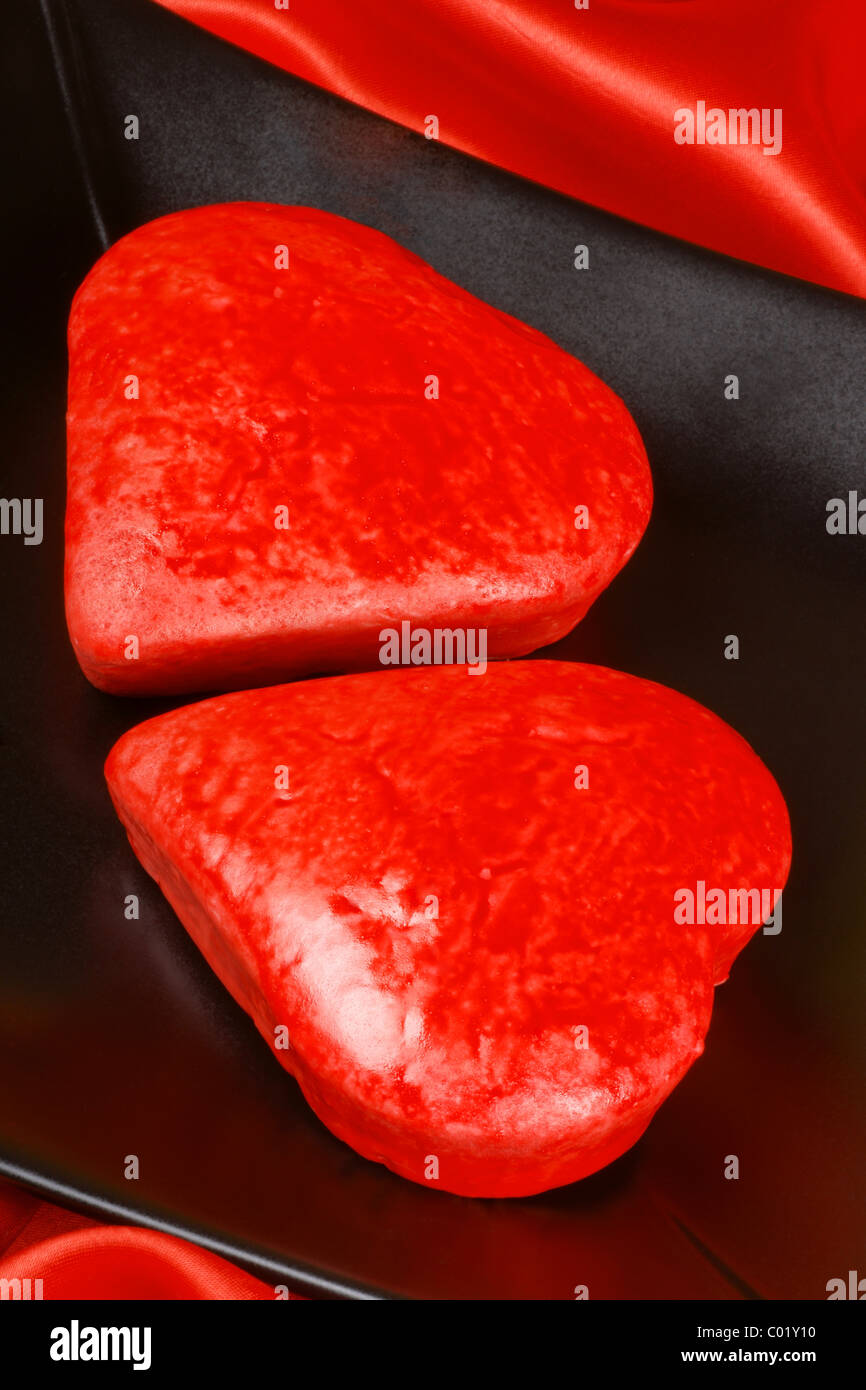 Two red heart shaped cakes on a black plate over a red background for ...