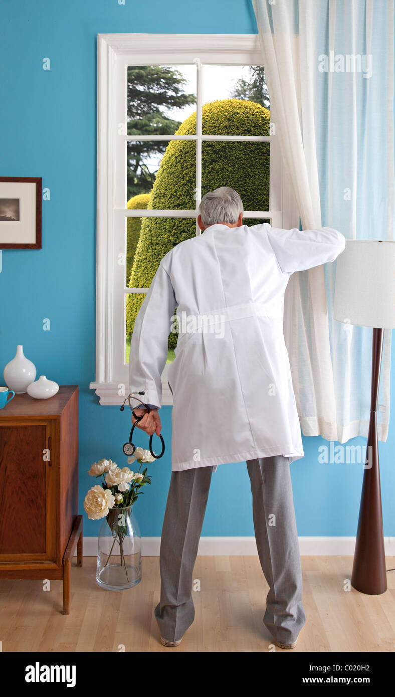 Male doctor in house peeks out window at giant topiary. Stock Photo