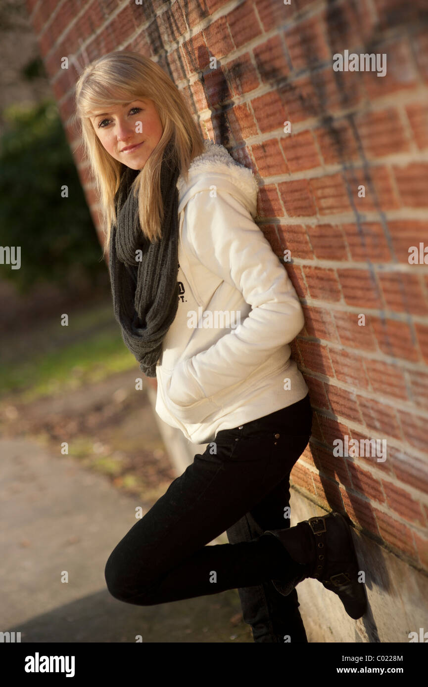 A slim blonde 14 year old teenage girl lesning on a brick wall, UK Stock Photo