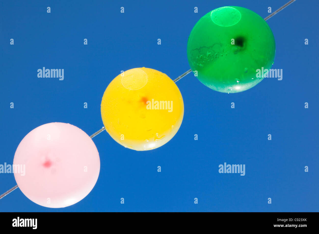 Colored balloons with water-drops hanging on a clothesline with a blue sky as background, from below Stock Photo