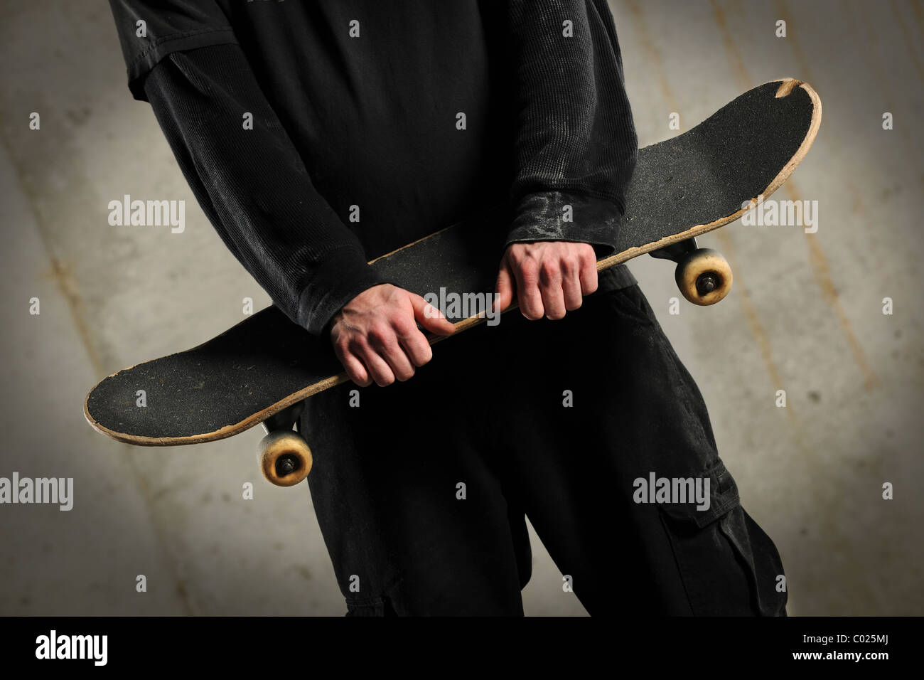 Mid section of man holding skateboard over concrete background with spotlight Stock Photo