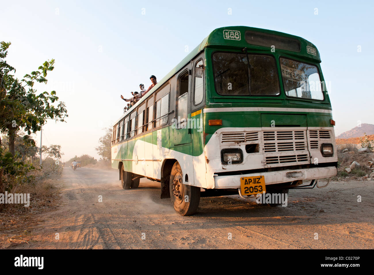 Indian bus traveling along a country road with people sitting on the roof. Andhra Pradesh, India Stock Photo