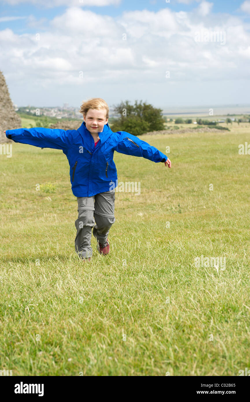 Young girl in outdoor clothing running across a field into a strong wind with her arms outstretched. Stock Photo