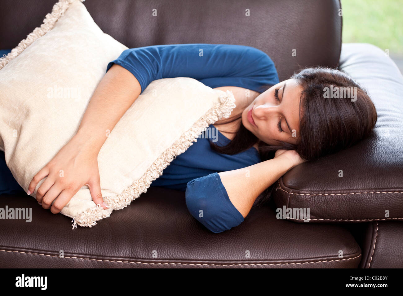 Young woman lying on a leather sofa, sleeping with a pillow in her arms