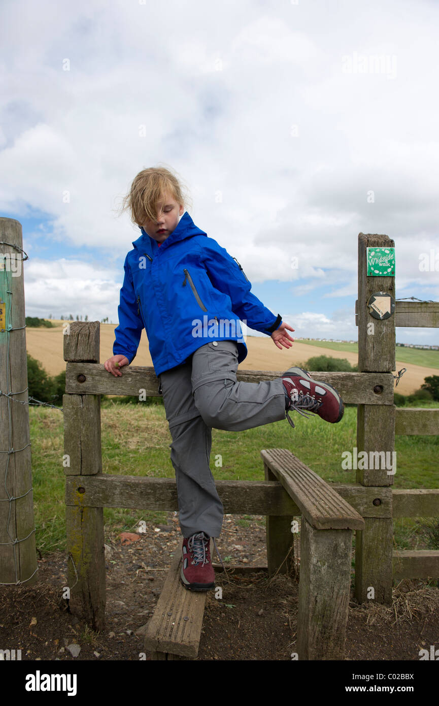 Young girl in outdoor clothing, climbing over style on a walk in the