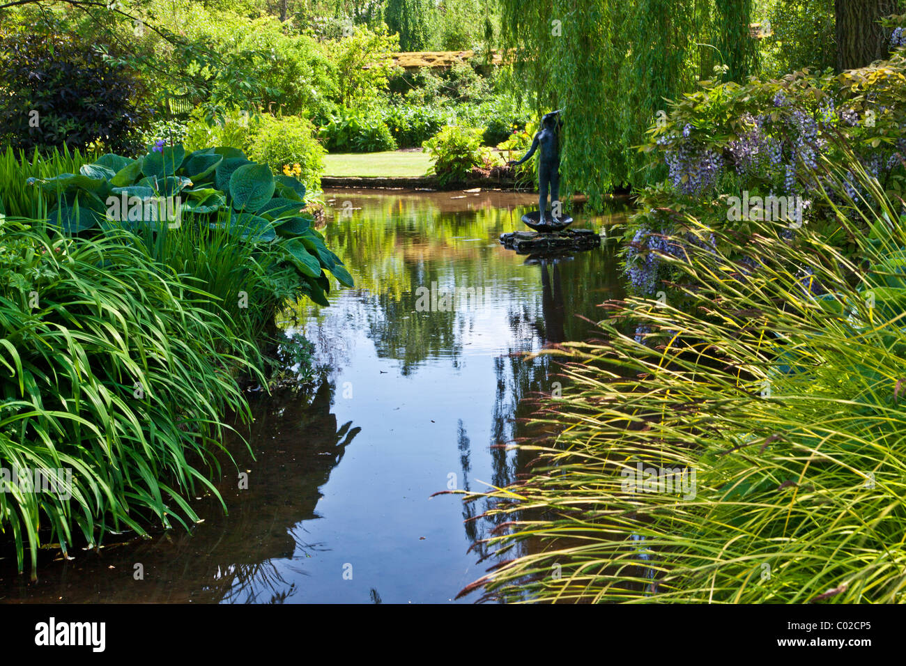 An ornamental garden pond in an English country garden with statue,ferns, and a weeping willow. Stock Photo