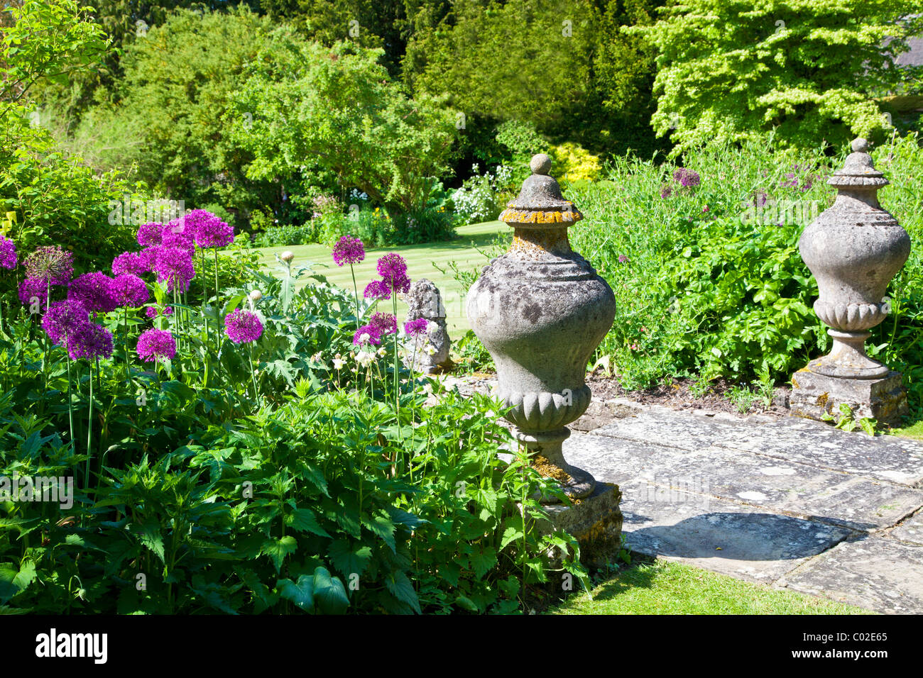 Stone garden ornaments and purple allium or onion flowers overlooking a lawn in an English country garden in summer Stock Photo